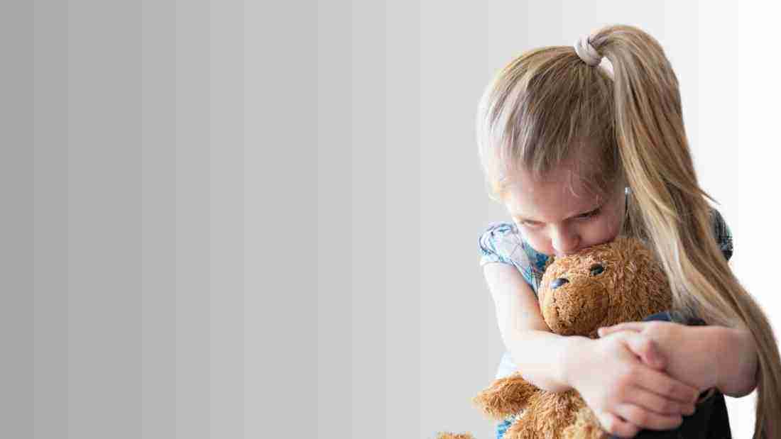 Sad little girl clutching a teddy bear
