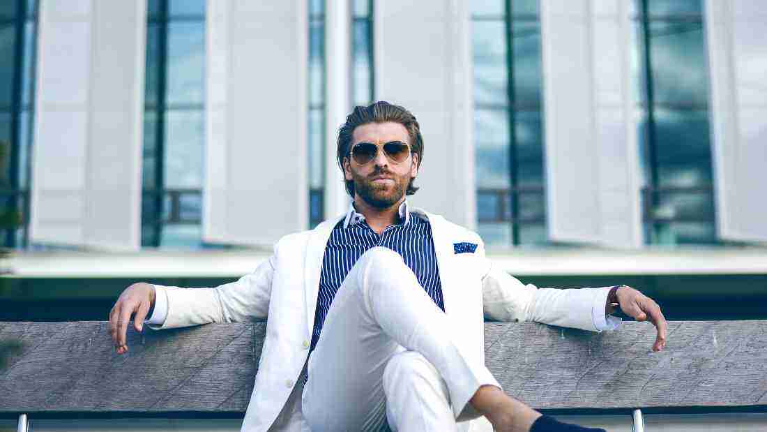 An arrogant man in a white suit sitting on a bench