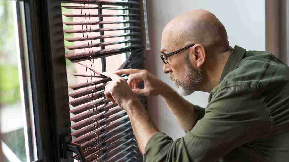 A man peeping through the blinds to spy on his neighbors