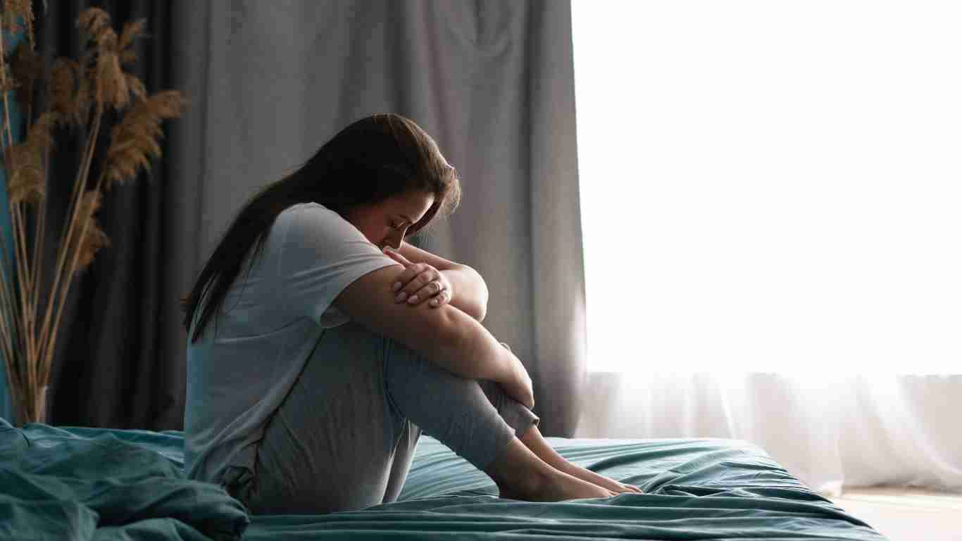 A depressed woman crouched on a bed