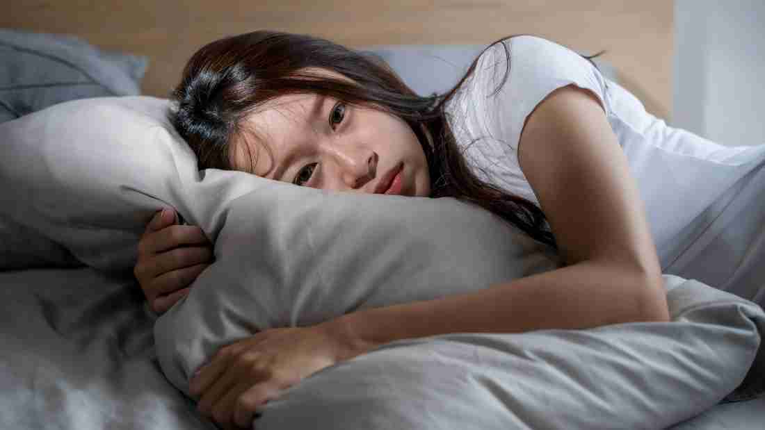 A depressed young woman lying on a bed
