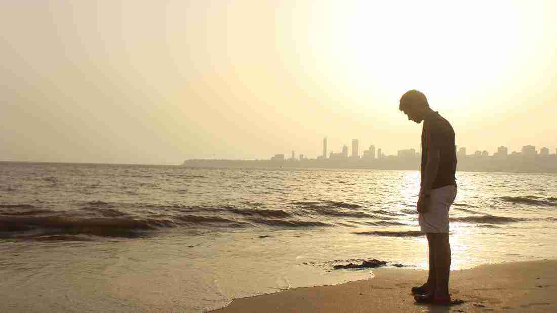 A lonely young man walking on the beach at sunset