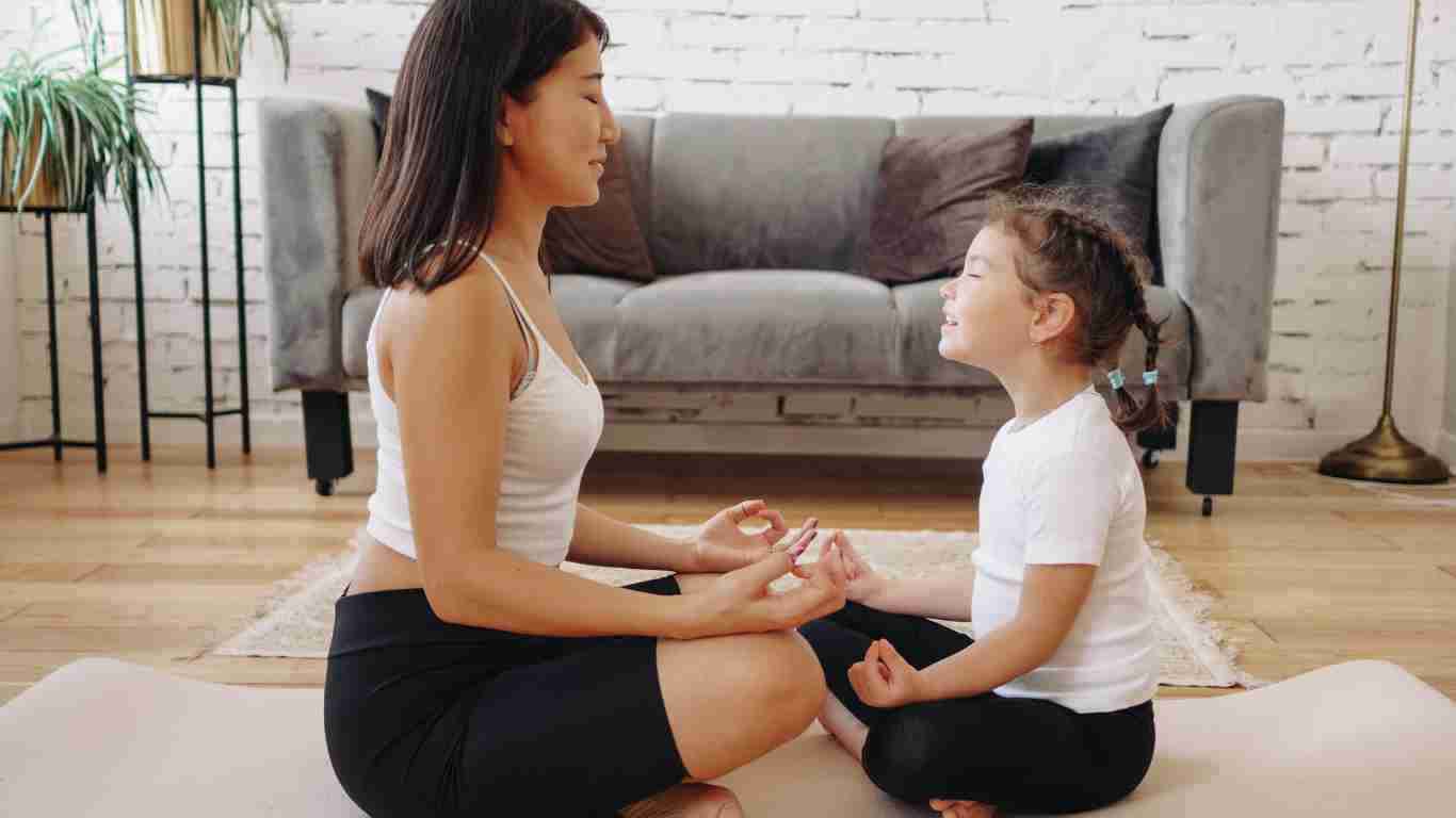 A mother and her young daughter meditating in their living room
