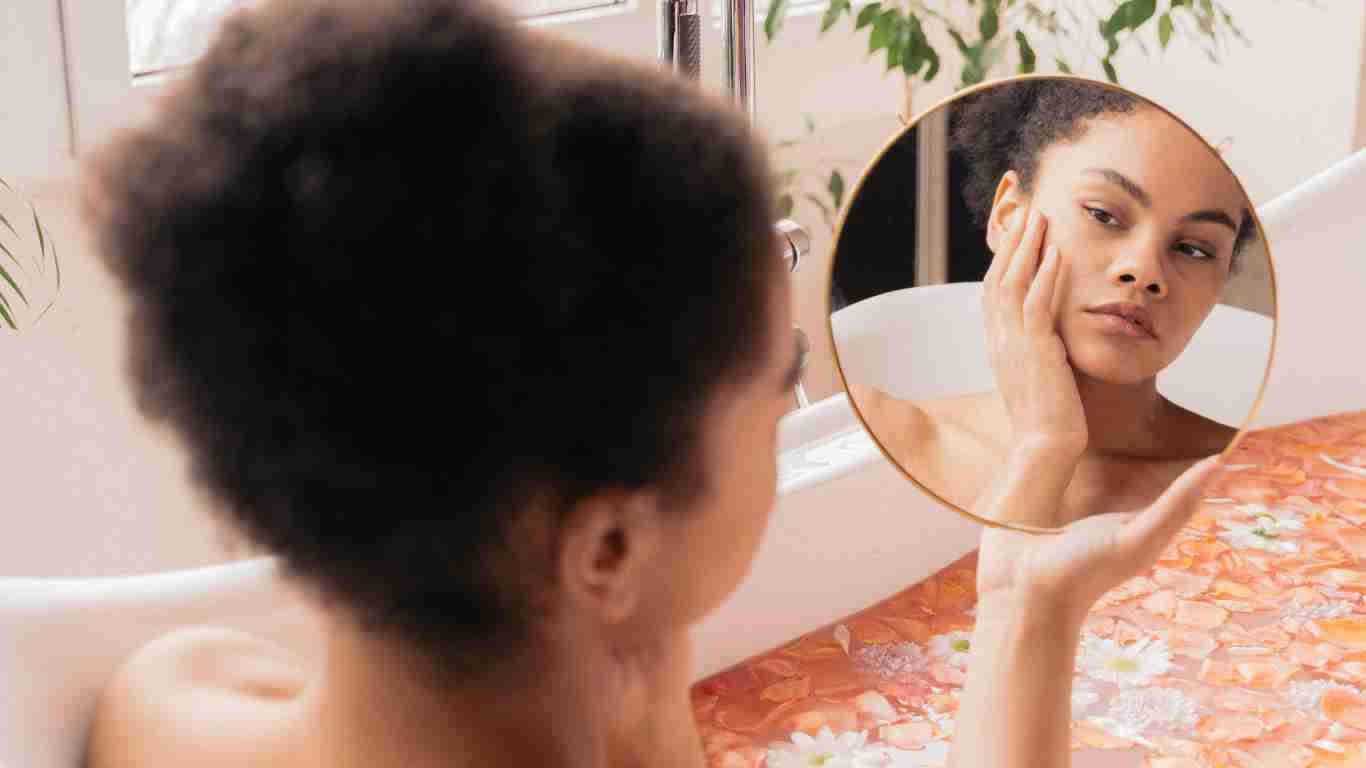 A woman gazing in a mirror as she takes a bath