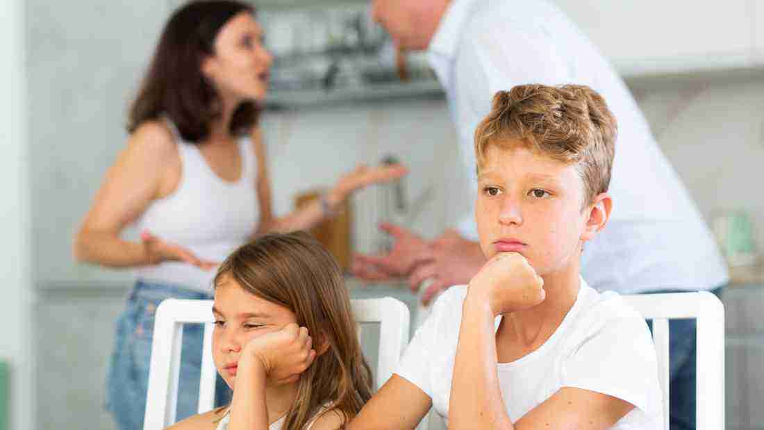 Children sitting quietly as their parents argue in the background