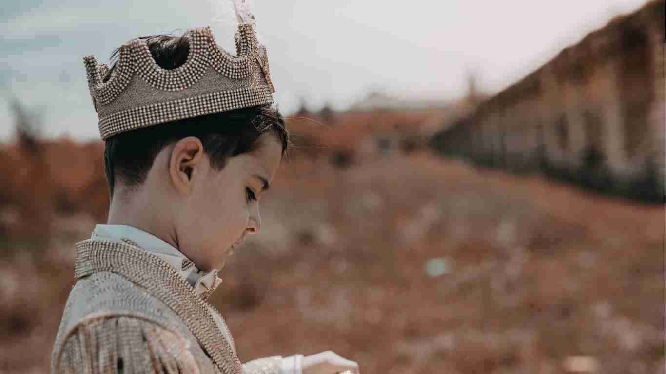A little boy dressed as a prince and wearing a crown