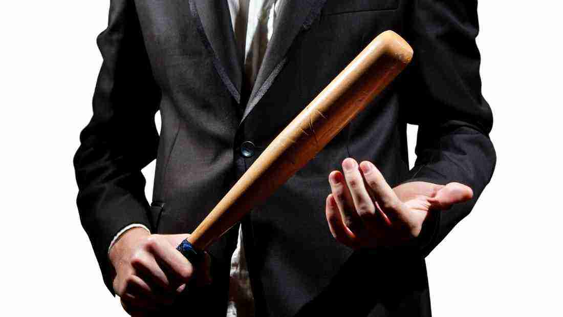 A man in a suit, holding a baseball bat in a threatening manner
