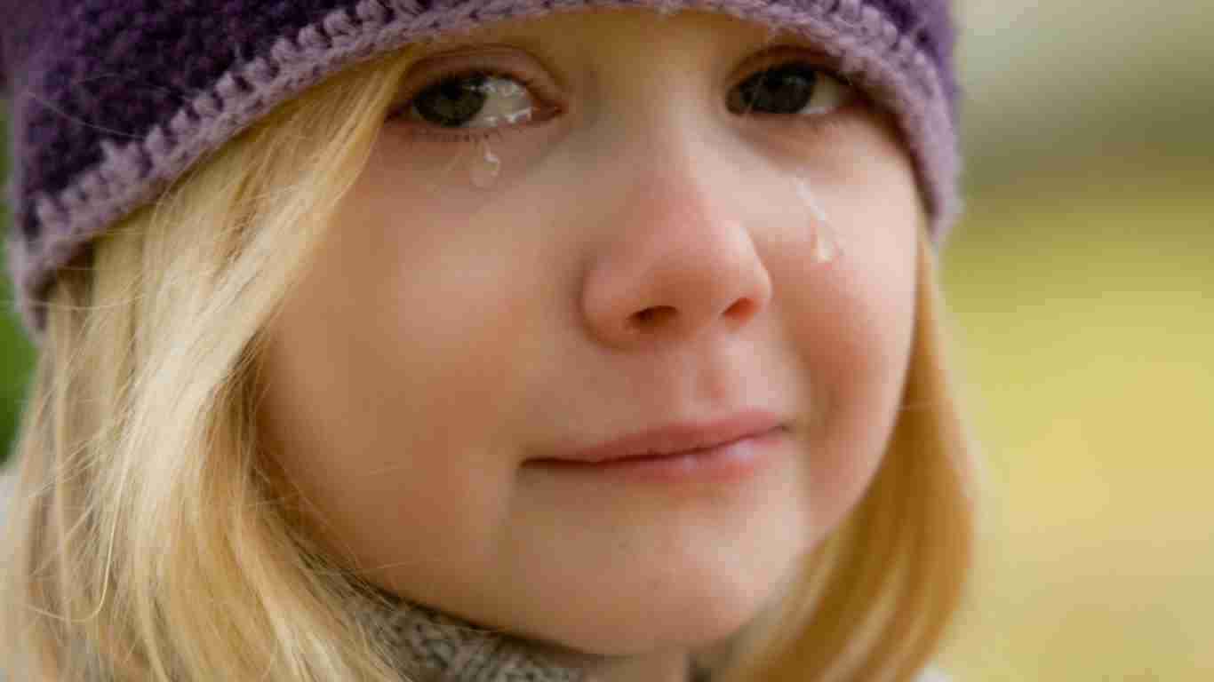 A little girl wearing a beanie. Tears are streaming down her face.