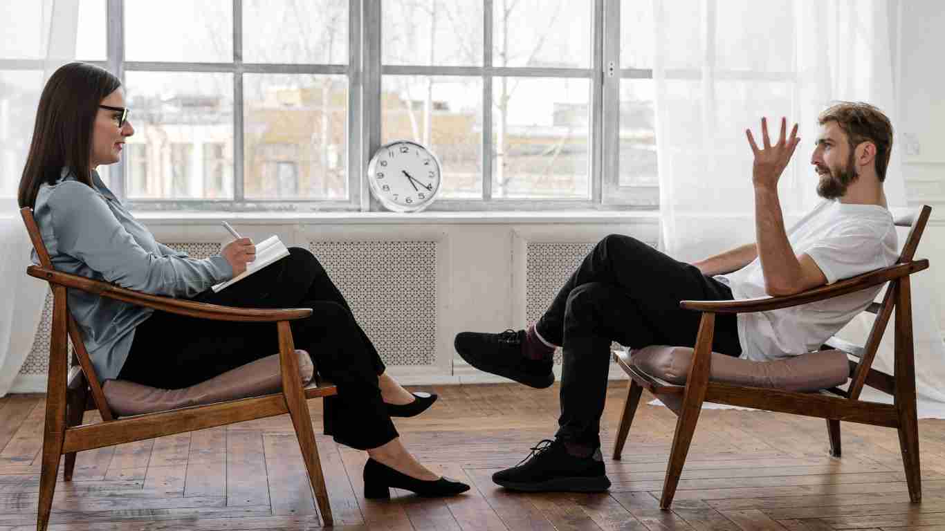 A man sitting in an armchair explaining something to his therapist during a therapy session