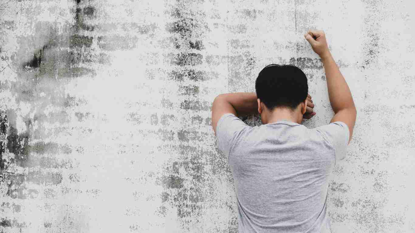A distraught man leaning against a brick wall