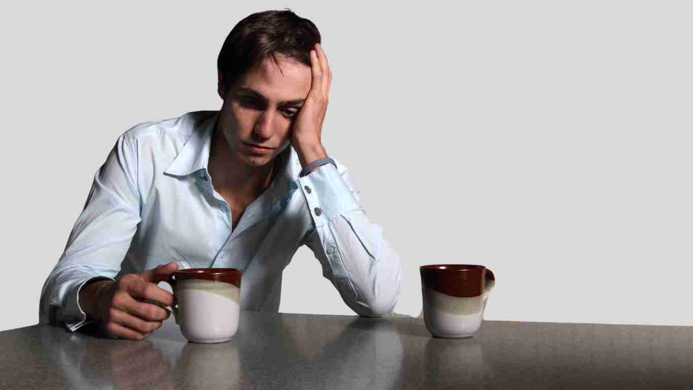 An unhappy man sitting alone at a table with two mugs
