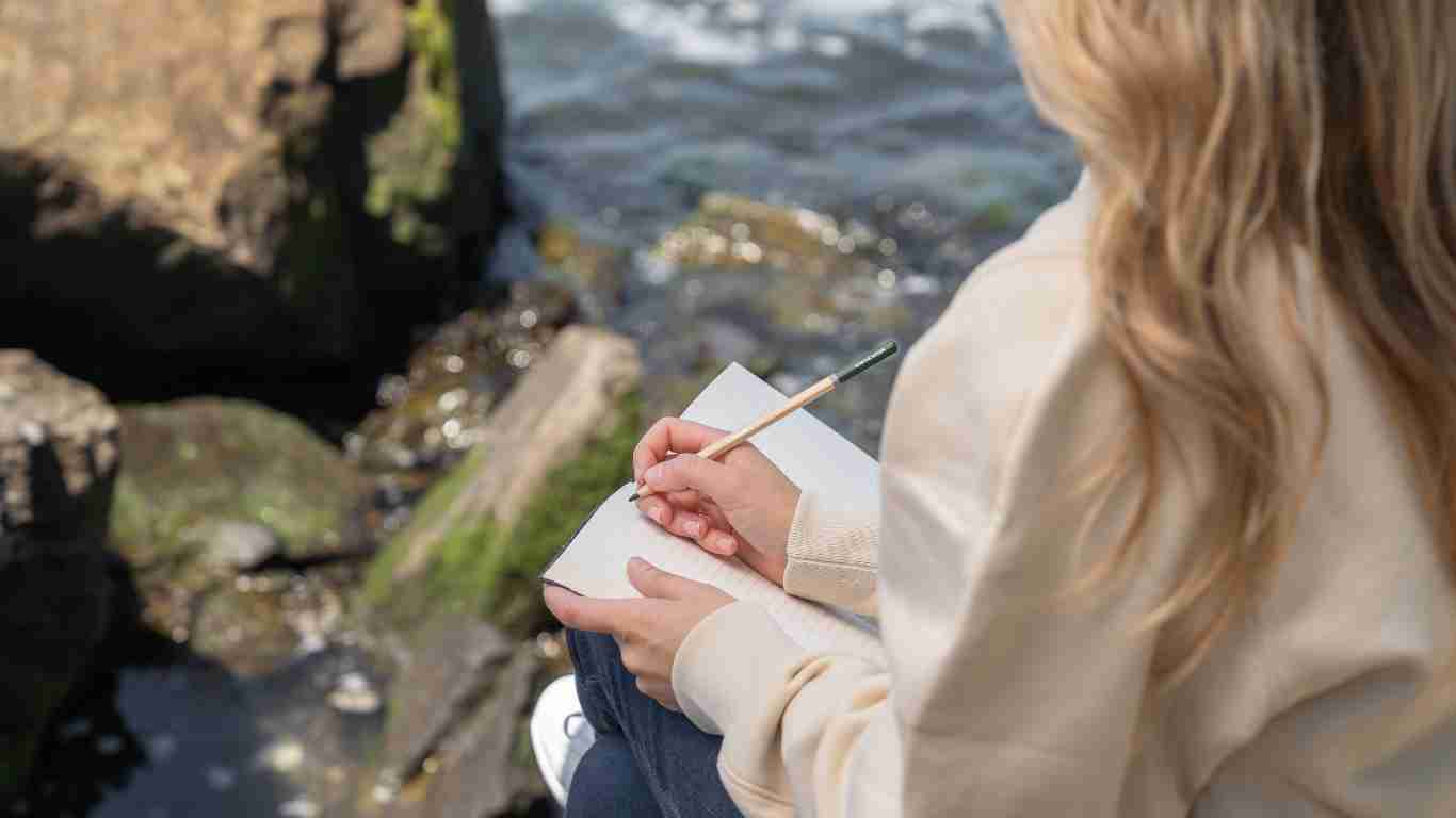 A young woman journaling as she sits by a stream