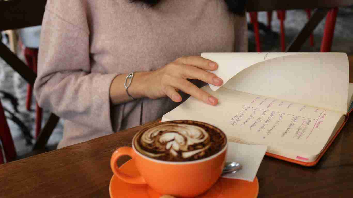 A woman writing in her journal while drinking coffee in a coffee shop