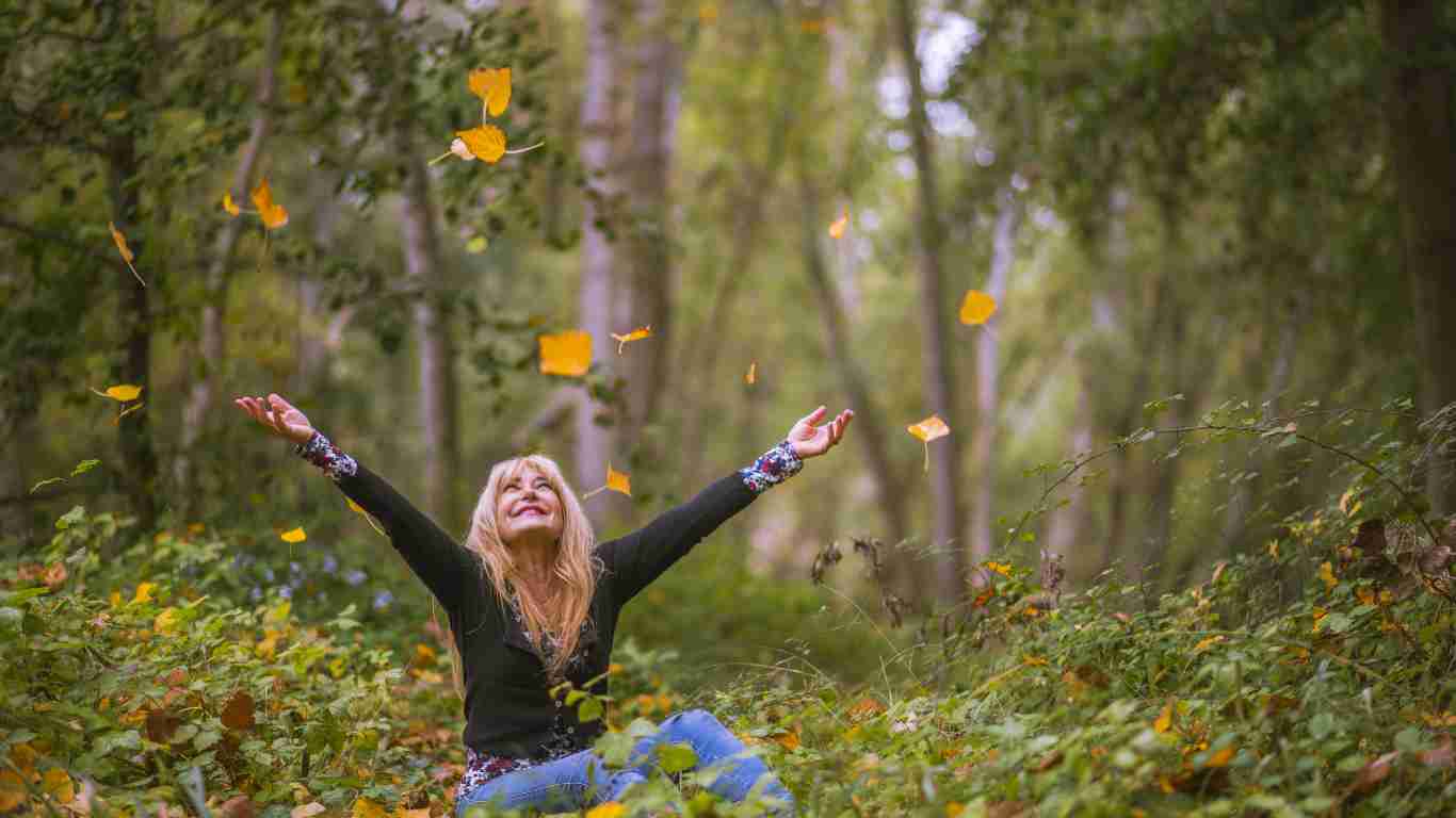A woman enjoying the leaves falling from trees in a forest