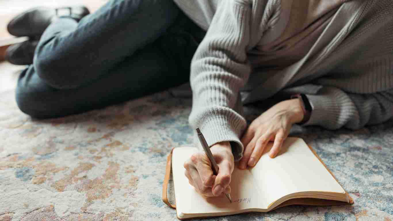 A woman lying on the floor as she writes in her self love journal